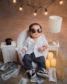 a young boy wearing sunglasses sitting on top of a chair next to money and a lamp