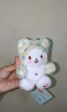 a hand holding a small white teddy bear with blue spots on it's face