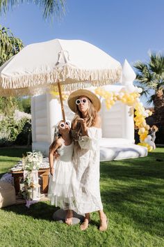 a woman in a white dress and straw hat standing under an umbrella on the grass