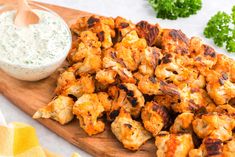 a wooden cutting board topped with tater tots next to a bowl of ranch dressing