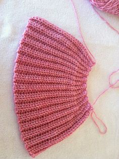 a pink crocheted hat sitting on top of a white blanket next to a ball of yarn