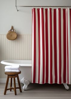 a red and white shower curtain next to a bath tub with towels on the floor