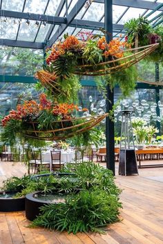 the inside of a greenhouse with plants and flowers hanging from it's ceiling, surrounded by tables and chairs