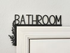 a bathroom sign hanging on the side of a wall next to a white door with black trim