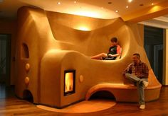 two men sitting on a bench in front of a fake mushroom like house with a fireplace