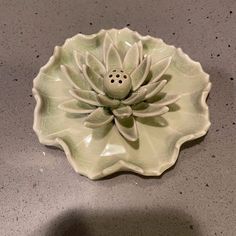 a white ceramic flower dish sitting on top of a gray counter next to a black object