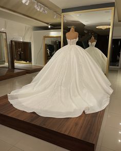 a white wedding dress on display in front of a mirror and mannequins