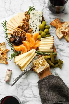 cheese, crackers and olives are arranged on a marble table with two glasses of wine