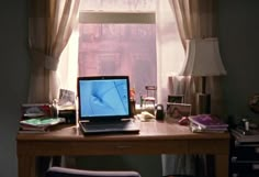 an open laptop computer sitting on top of a wooden desk in front of a window