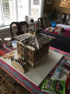 there is a cake that looks like a house on top of a table with chairs