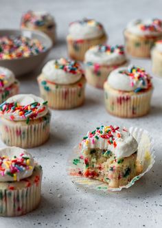 cupcakes with white frosting and sprinkles are on the table