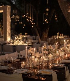 a long table is set with candles and plates for an elegant wedding reception at night