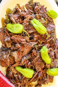 a white plate topped with shredded beef and green peppers on top of a red towel