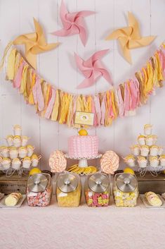 the dessert table is decorated with pink, yellow and white paper cranes hanging over it