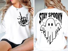 a woman sitting on top of a bed wearing a white shirt that says stay spooky