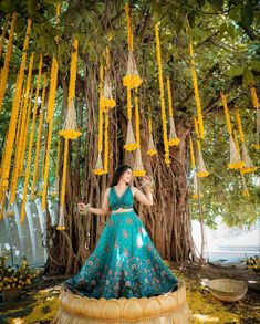 a woman in a blue dress standing under a tree with yellow flowers hanging from it