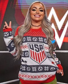 a woman with grey hair wearing a red and white sweater is standing in front of a wrestling ring