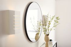 two vases with flowers sit on a table in front of a mirror and shelf