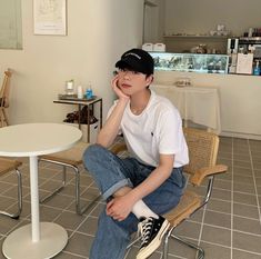 a young man sitting on top of a chair next to a white table in a room