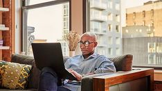 an older man sitting on a couch with a laptop in his lap and looking at the screen