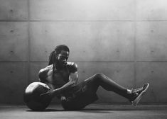 a man with dreadlocks sitting on the ground holding a medicine ball in his right hand