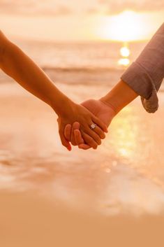 two people holding hands while walking on the beach