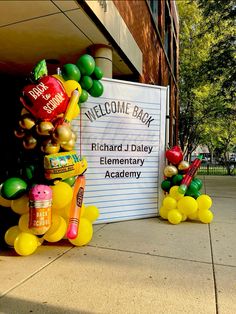 some balloons are sitting in front of a welcome back sign on the side of a building