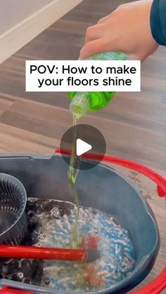 a person is pouring water into a pot with red handles on the floor and another person's hand holding a green bottle