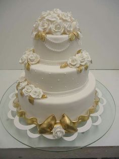 a three tiered wedding cake with white and gold flowers on the top, sitting on a glass platter