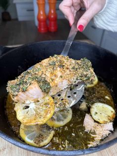 someone is cutting up some food in a pan with lemons and herbs on it