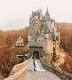 a bride and groom standing in front of an old castle on a cobblestone road