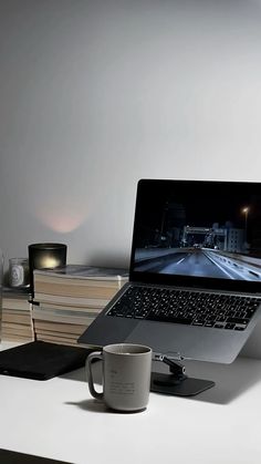 an open laptop computer sitting on top of a desk next to a cup and books