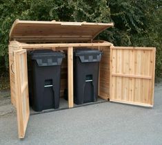 two black trash cans are in the back of a wooden storage shed with doors open