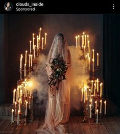 a woman standing in front of a bunch of candles with her wedding dress draped over