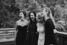 four women laughing together on a bridge in black and white, with trees in the background