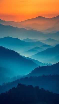 an orange and blue sunset over mountains with mist in the foreground, as seen from above