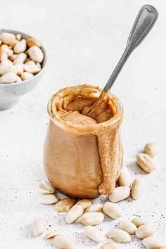 a jar filled with peanut butter next to two bowls full of nuts and spoons