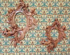 two carved wood frames on a wall with an ornate pattern in the backround