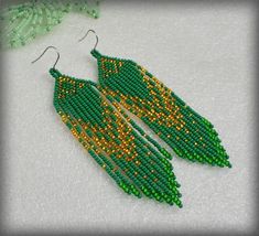 green and gold seed beaded earrings on white fabric with beads in the shape of leaves