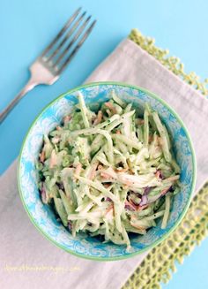 a blue and white bowl filled with coleslaw on top of a table next to a fork