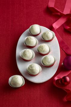 cupcakes with white frosting on a plate next to red ribbon and ornaments