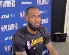 the lakers player is sitting in front of a blue wall and wearing a black shirt