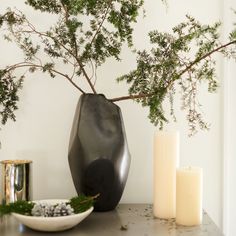 a black vase sitting on top of a table next to two candles and a bowl