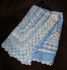 a blue and white crocheted blanket laying on top of a black couch next to a remote control