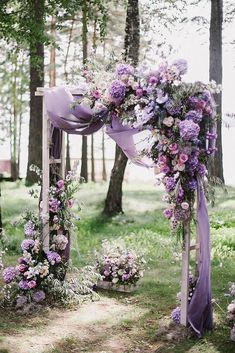 an outdoor wedding setup with purple flowers and greenery on the ground, surrounded by trees