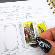 a hand holding a playing card next to an open book with writing on the pages