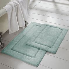 two bath mats sitting next to each other on the floor in front of a tub