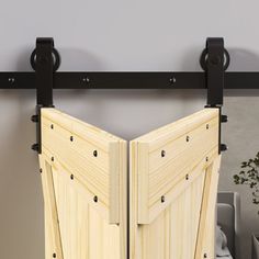 an open wooden door with black hardware on the bottom and side, in front of a gray wall