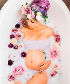 a pregnant woman in a bathtub with flowers on her head and hands under her belly