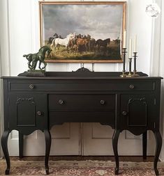 a painting hangs above a black desk in a room with white walls and an antique rug